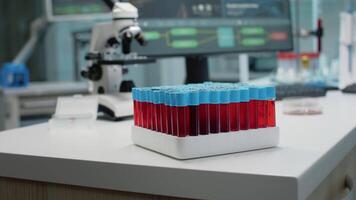Close up of vacutainers with blood or red liquid in laboratory on desk. Tray of glass test flasks for dna prepared for fluid analysis. Medical equipment and microscope for development video