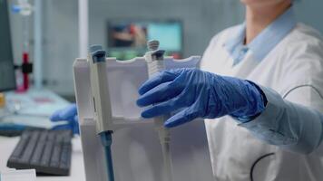 Close up of biochemist using micropipette in laboratory for scientific analysis in healthcare industry. Professional doctor in lab coat with liquid dropper on desk used for development video