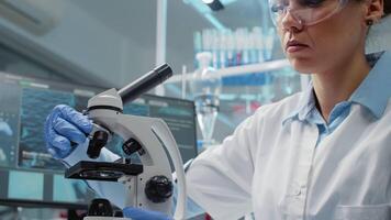 Portrait of scientific woman using microscope in laboratory with magnifying glass and optical lens. Doctor with lab coat, glasses and gloves operating research instrument for dna analysis video