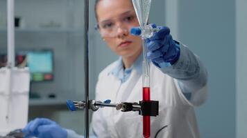 Close up of scientist using laboratory glassware on desk for medical experiment. Biochemistry doctor mixing blood in test tube with solution from chemical dripping pipe for development video
