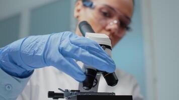 Close up of scientist checking microscopic tool with sample tray in laboratory. Woman using microscope with magnifying lens used for optical dna investigation in medical research industry video