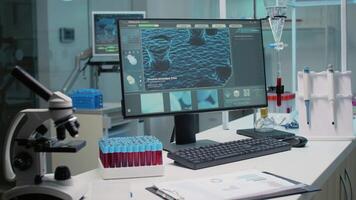 Nobody at chemistry desk in laboratory workplace with medical equipment for research innovation. Empty scientific room with animation on computer, microscope and vacutainers for science video