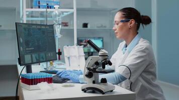 Researching doctor in laboratory using chemical tools for investigation. Scientist woman typing on computer and looking at bacteria in petri dish while having professional equipment on desk video