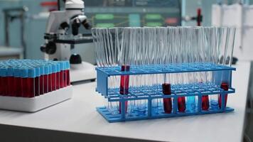 Close up of laboratory test tubes with blood on desk at workplace. Glass flasks filled with red substance or liquid placed on chemical tray. Vacutainers and microscope used in microbiology video