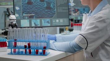 Medicine scientist using computer while holding test tube with red liquid solution for research development. Biochemistry woman with protection glasses and gloves studying lab flask video