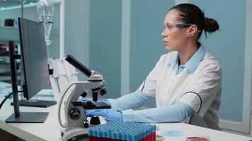Researching specialist working in laboratory with chemical equipment. Woman using computer for dna examination while having microscope, petri dish, vacutainers and micropipette on desk video