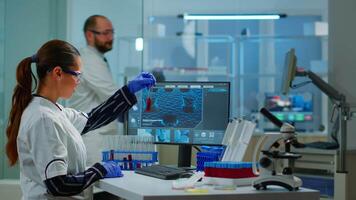 Chemistry doctor analysing blood sample and typing on computer while coworker opening door using digital computer with touch scan. Woman examining virus evolution using high tech and chemistry tools video