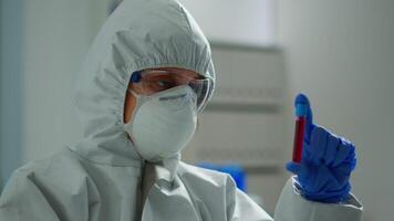 Scientist in coverall doing research analysing liquid in tube at modern equipped laboratory. Biochemist examining vaccine evolution using high tech for treatment development against covid19 virus video