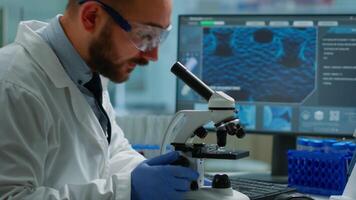 Male scientist looking under microscope in medical development laboratory, entering data in computer. Specialists working on medicine, biotechnology research in advanced pharma lab video