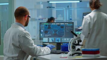 Scientist man examining blood samples and liquid working in modern equipped laboratory. Team of doctors analysing vaccine evolution using high tech researching diagnosis against covid19 video