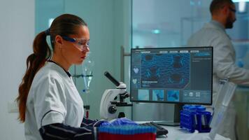 Biotechnology scientist researching in laboratory using microscope and typing on pc. Chemist examining virus evolution using high tech for scientific research of vaccine development against covid19 video