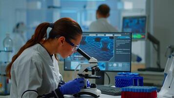 Scientist looking at biological samples under microscope typing on pc. Team of chemists working in lab, examining virus evolution using high tech for scientific research of vaccine development. video