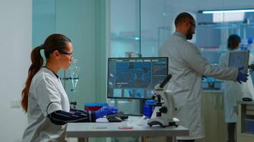 Team working to develop a new vaccine in modern equipped laboratory, woman typing at computer. Group of biochemistry scientists examining virus evolution using high tech for researching treatment video