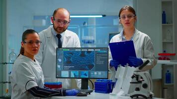 Team of scientists sitting in laboratory looking at camera in modern equipped lab. Group of doctors examining virus evolution using high tech for scientific research, vaccine development. video