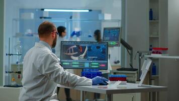 Medical scientist working with DNA scan image in modern equipped laboratory holding test tube with sample. Team examining vaccine evolution using high tech and chemistry tools for vaccine development video