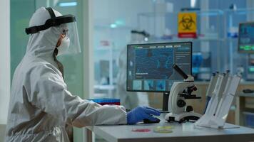Tired laboratory doctor with overall suit working at computer and looking at camera. Scientist examining virus evolution using high tech, chemistry tools for scientific research, vaccine development video