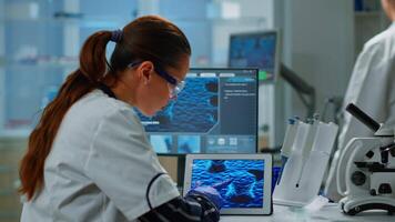 Scientist using digital tablet working in modern medical research laboratory, analyzing DNA information. Medicine, biotechnology research in advanced pharma lab, examining virus evolution video