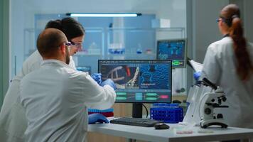 grupp av vetenskapsmän arbetssätt i modern utrustad laboratorium pekande på dator skrivbordet. team av doktorer granskning vaccin Evolution använder sig av hög tech forska diagnos mot covid19 virus video