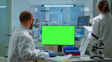 Man researcher looking at chroma key display in modern equipped lab typing on computer. Team of microbiologists doing vaccine research writing on device with green screen, isolated, mockup display. video