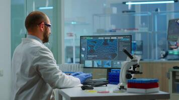 Man biologist checking DNA informations typing on pc in modern equipped laboratory. Scientists examining vaccine evolution in medical lab using high tech, chemistry tools for scientific research. video
