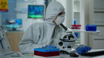 Woman scientist in ppe suit working in lab using modern microscope with slides. Team of chemists researcher examining virus evolution using high tech for vaccine scientific research against covid19 video