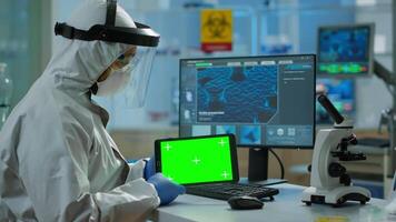 Doctor with coverall working at tablet with green screen in modern equipped lab. Team of microbiologists doing vaccine research writing on device with chroma key, isolated, mockup display. video