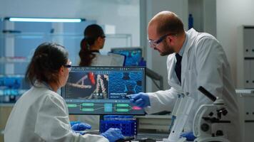 team av vetenskapsmän orolig handla om virus Evolution diskuterar i utrustad laboratorium pekande på dator. grejer granskning vaccin utveckling använder sig av hög tech forska behandling mot covid19 virus video