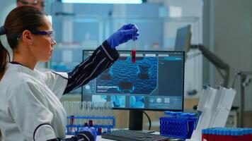 Scientist doctor looking at blood sample and typing on computer while coworker opening door using digital computer with touch scan. Woman examining virus evolution using high tech and chemistry tools video