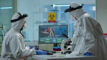 Biotechnology scientist wearing ppe suit researching in equipped laboratory. Chemists examining virus evolution on pc using high tech for scientific research of vaccine development against covid19 video