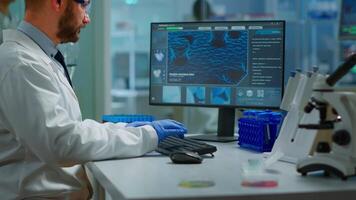 Portrait of scientist man looking at camera sitting in modern equipped laboratory. Scientist doctor examining virus evolution using high tech typing on computer chemistry tools for scientific research video