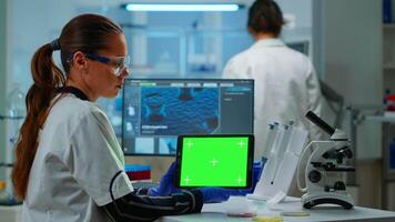 medicinsk forskning forskare arbetssätt på läsplatta med grön skärm falsk upp mall i applicerad vetenskap labb. ingenjörer ledande experiment i bakgrund, granskning vaccin Evolution använder sig av hög tech video