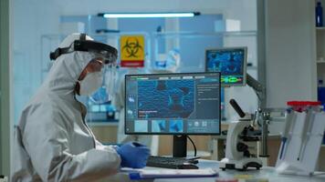 Scientist in protection suit typing on pc working in medical laboratory, writing on clipboard, developing inovative drugs against new virus. Doctor using high tech, chemistry tools for researching video
