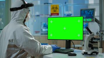 Man researcher in coverall looking at chroma key computer in modern equipped lab. Team of microbiologists doing vaccine research writing on device with green screen, isolated, mockup display. video