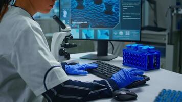 Biochemist using microscope and writing at computer sitting in equipped laboratory. Scientist doctor working with various bacteria, tissue, blood samples, pharmaceutical research for antibiotics video