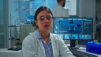 Outbreak chemist sitting in modern equipped lab looking tired at camera, yawning. Scientist examining virus evolution using high tech and chemistry tools for scientific research, vaccine development video