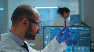 Viorolog researcher examining blood sample from test tube working in modern equipped laboratory. Scientist man analysing vaccine evolution using high tech researching diagnosis against covid19. video
