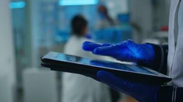 Close up of scientist examining datas from tablet while team of biologists doing biological researches in backgorund, analysing vaccine evolution using high tech for diagnosis against covid19 virus video