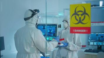Worried scientists in ppe suit talking behind the glass wall working in danger area of lab. Chemists developing vaccine using tablet examining virus evolution researching for treatment against covid19 video