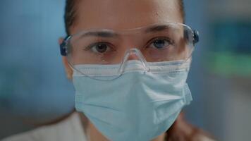 Chemist wearing face mask and protective goggles for safety in science laboratory. Microbiology specialist doing virus research and experiment for development during pandemic. Close up video