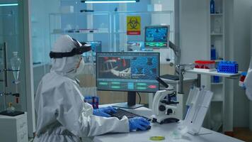 Chemist doctor in ppe suit working at pc while lab technician bringing her blood samples. Team of scientists examining vaccine evolution with high tech for researching treatment against covid19 virus video