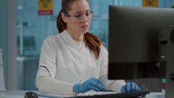 Science engineer working on computer and taking notes in laboratory. Biologist using technology to work on scientific experiment in lab and writing on paper to develop expertise. video