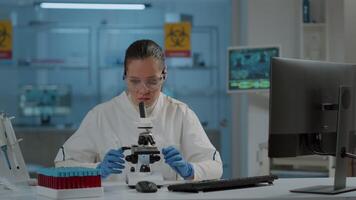 Lab worker using magnifying glass on microscope to work on science experiment. Woman chemist analyzing dna substance with microscopic lens on optical tool in laboratory. Biology researcher video