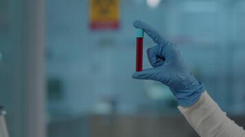 laboratorio lavoratore Tenere rosso sostanza nel test tubo per scienza analisi, Lavorando con dna nel laboratorio. chimica ingegnere con guanti utilizzando bicchiere borraccia per analizzare liquido nel cristalleria. vicino su video
