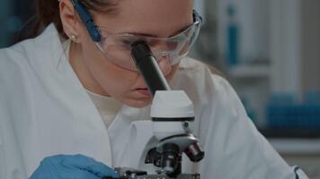 Scientist looking through microscopic lens to work on experiment, using microscope to analyze dna with selective focus in laboratory. Biologist working with magnifying glass. Close up video