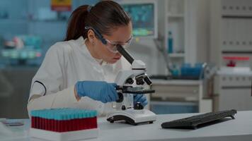 Portrait of scientist looking through microscopic lens in laboratory, working on experiment with magnifying glass. Woman using microscope and analyzing dna substance for development in lab. video