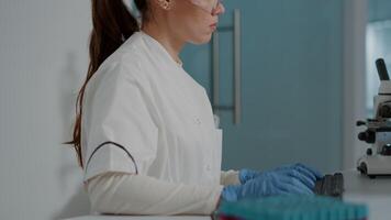 Biochemistry engineer using computer to work on scientific research in laboratory. Woman chemist wearing glasses and gloves, working with technology to develop science experiment. video