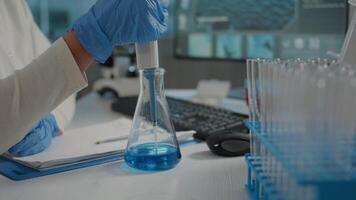 Scientist working with micro pipette and beaker to mix substance in test tube for biochemical experiment in laboratory. Researcher using scientific instruments and lab glassware. Close up video