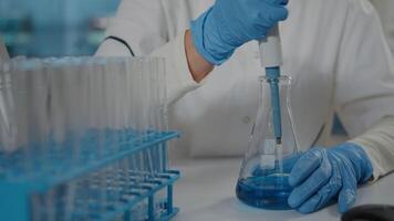 Specialist working with micro pipette to drop liquid in beaker and test tube. Chemistry engineer using laboratory equipment and glassware to do research experiment at work. Close up video
