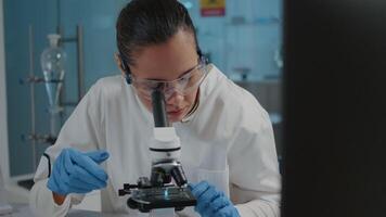 Portrait of scientist analyzing liquid sample on microscope tray in laboratory to research dna genetic. Lab worker with safety glasses using optical glass tool for scientific development. video