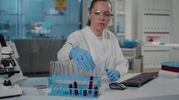 mikrobiolog analyserar testa rör med röd ämne i vetenskap labb, granskning flytande i flaska. kemist använder sig av laboratorium glas till do vetenskaplig experimentera, arbetssätt på utveckling. video